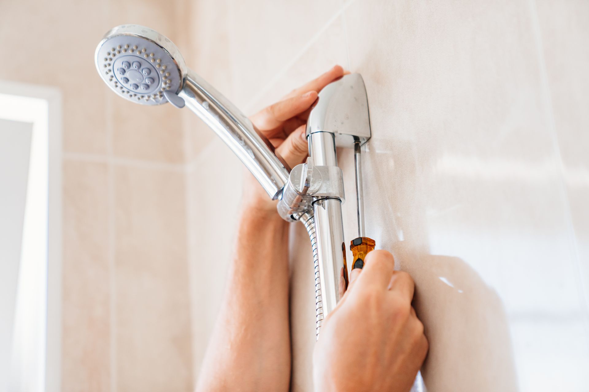 Hands adjusting a handheld showerhead mount on a tiled bathroom wall
