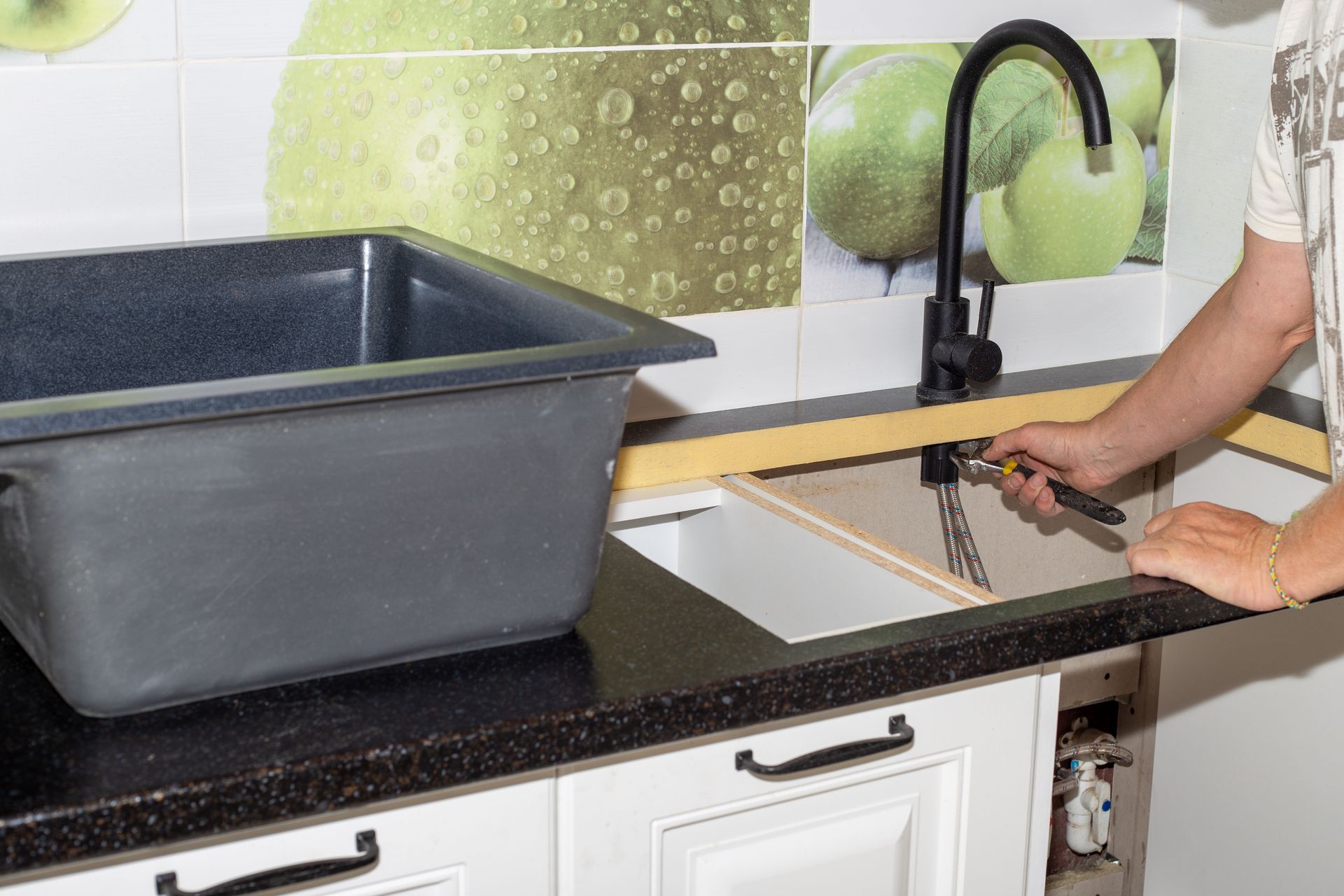 Person using a kitchen sink beside a large gray tub on a black countertop, with a faucet and tiled backsplash.