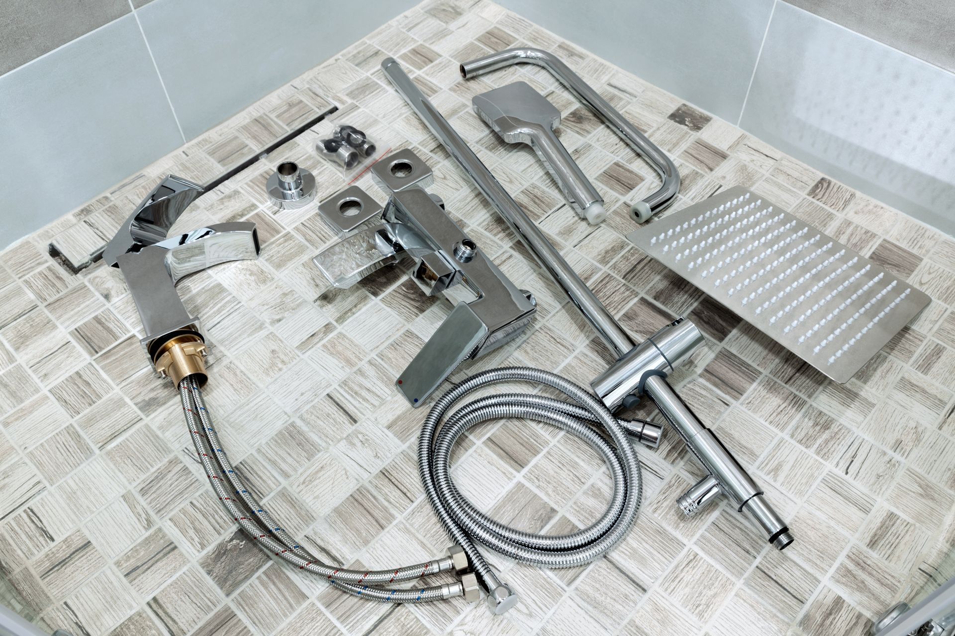 Assorted metal tools and hose parts laid out on newspaper in a tiled sink or shower area