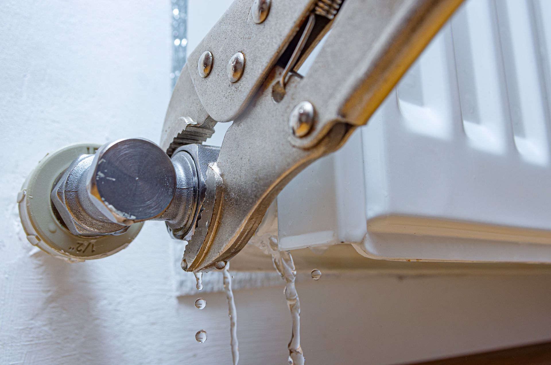 Pliers gripping a radiator valve as water drips from the pipe connection