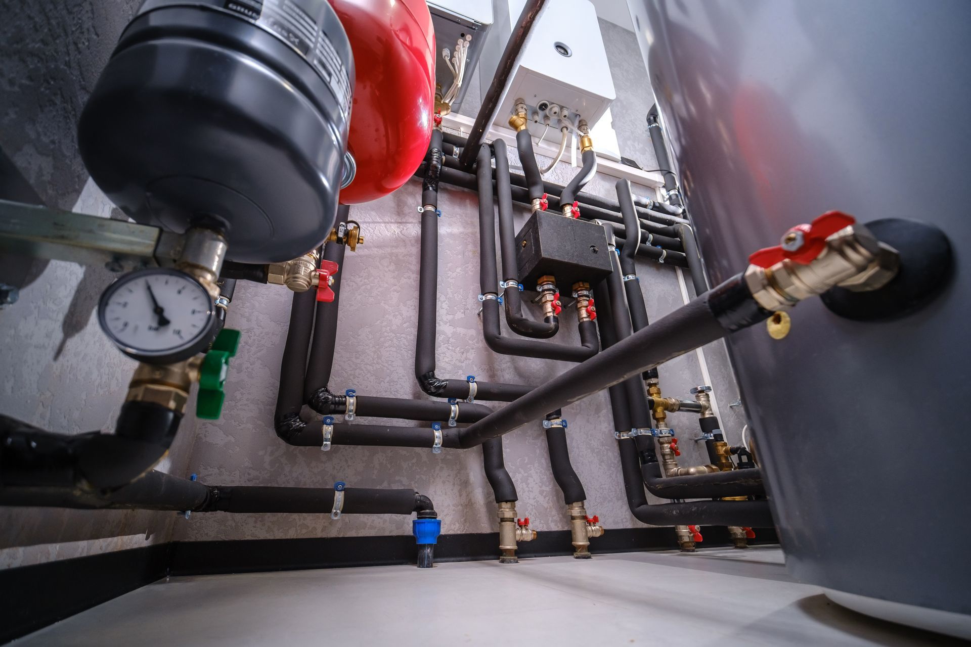 Industrial boiler room with pipes, valves, gauges, and red and black equipment against gray walls