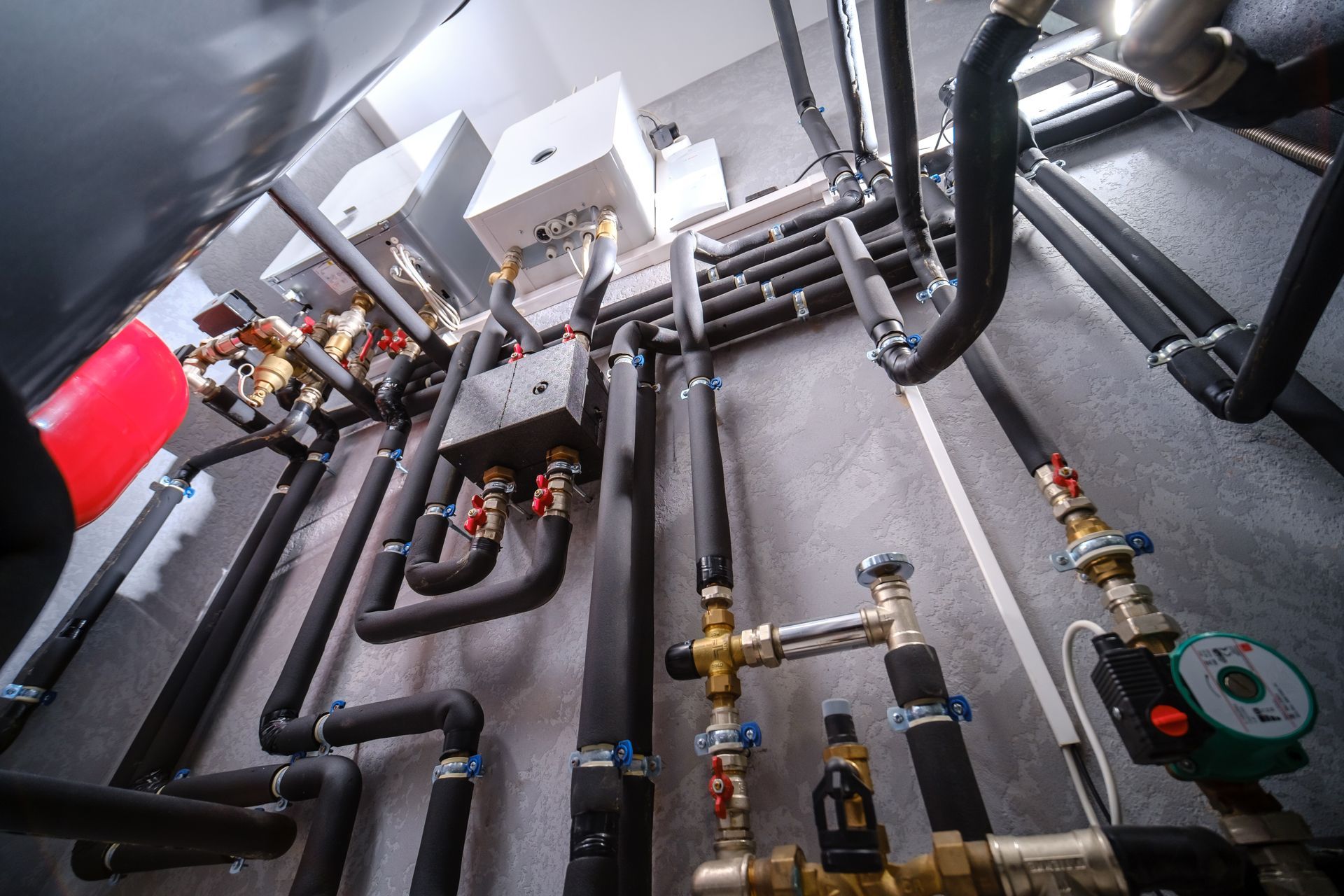 Basement utility room with pipes, valves, pumps, and electrical equipment on the floor and walls