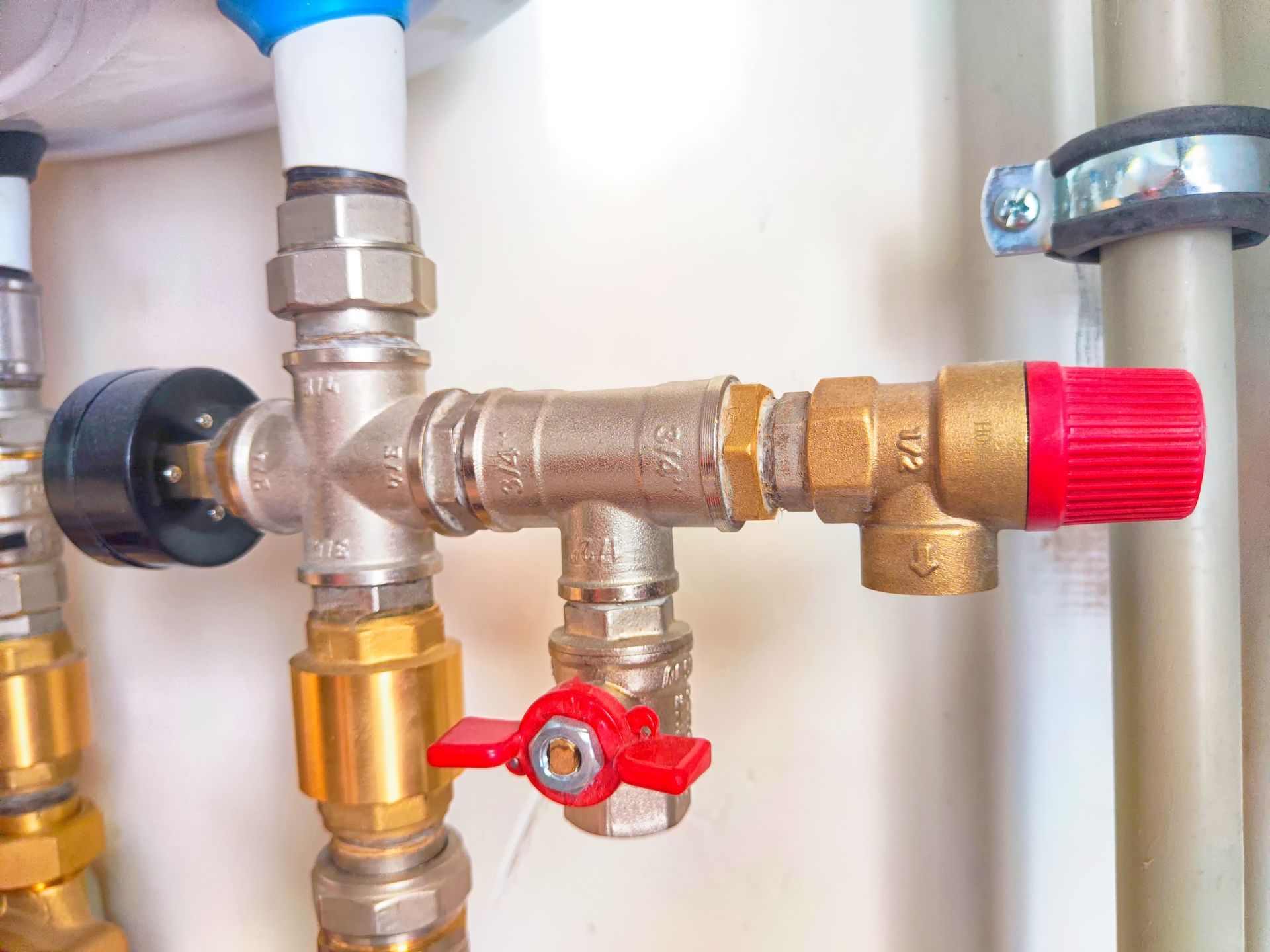 Plumbing manifold with brass valves, red handles, and white and blue pipes in a utility setting