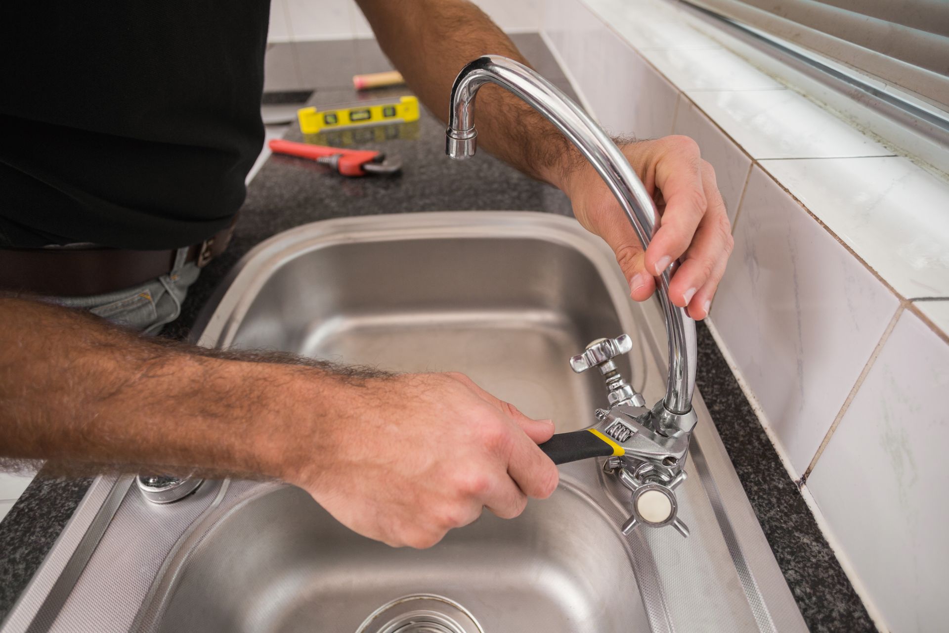 Person tightening a kitchen sink faucet with a wrench beside a stainless steel sink.