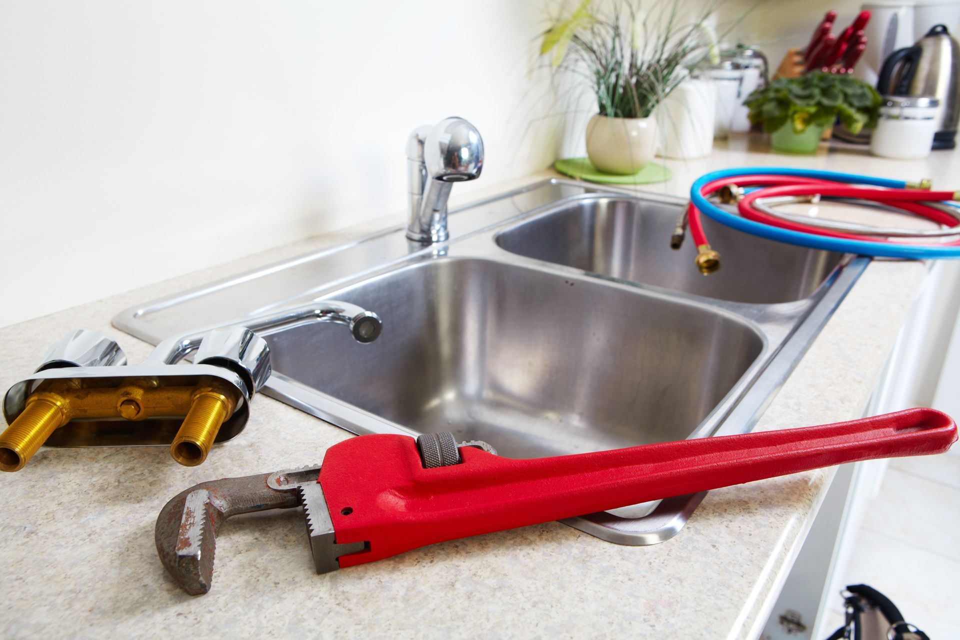Kitchen sink with red pipe wrench and other tools on the countertop