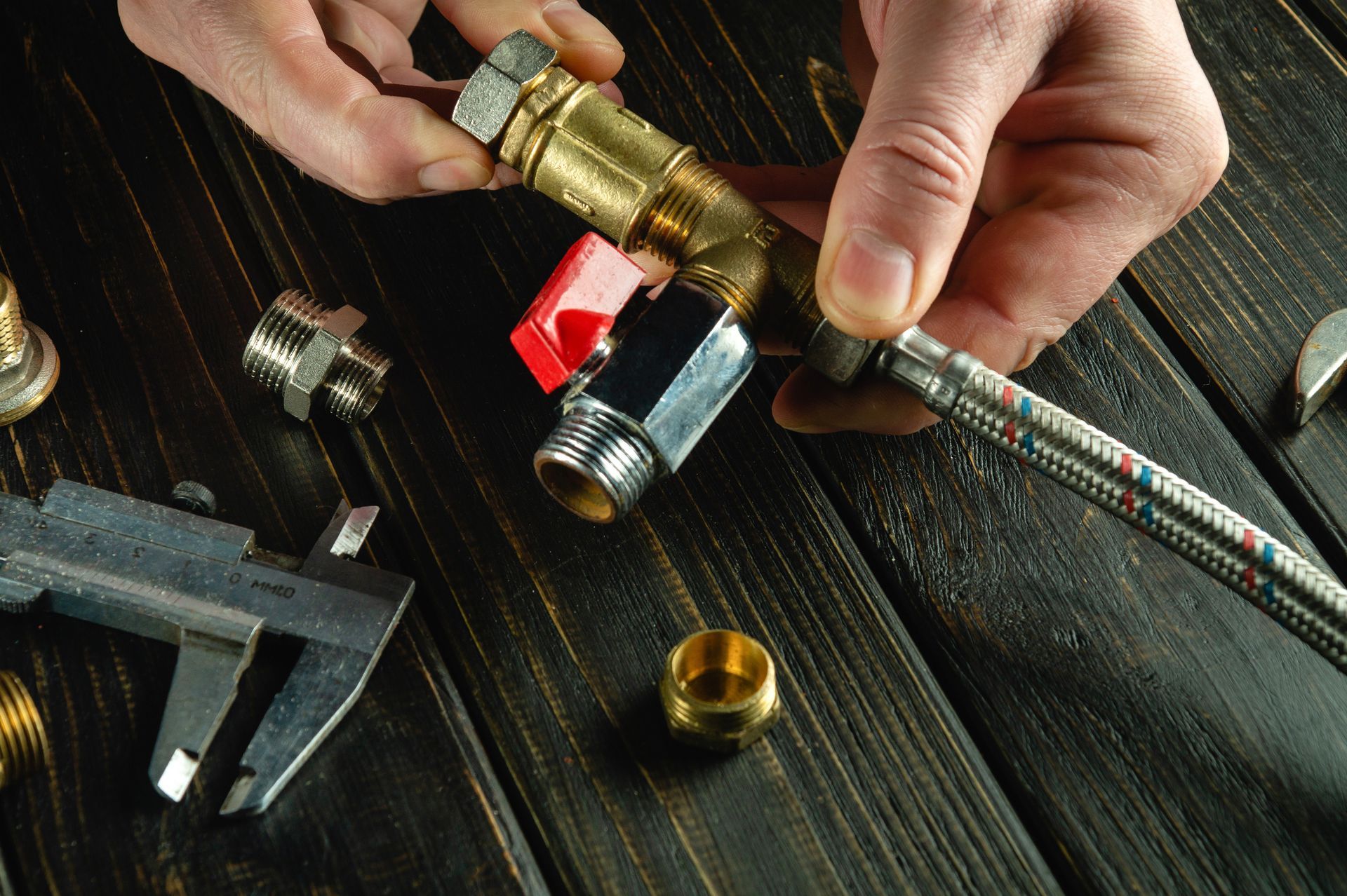 Hands connecting brass plumbing fittings with a wrench on a dark wooden surface