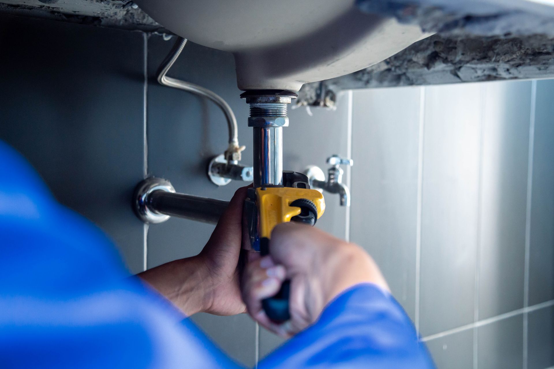 Plumber using a wrench to repair a bathroom sink drain under a white basin.