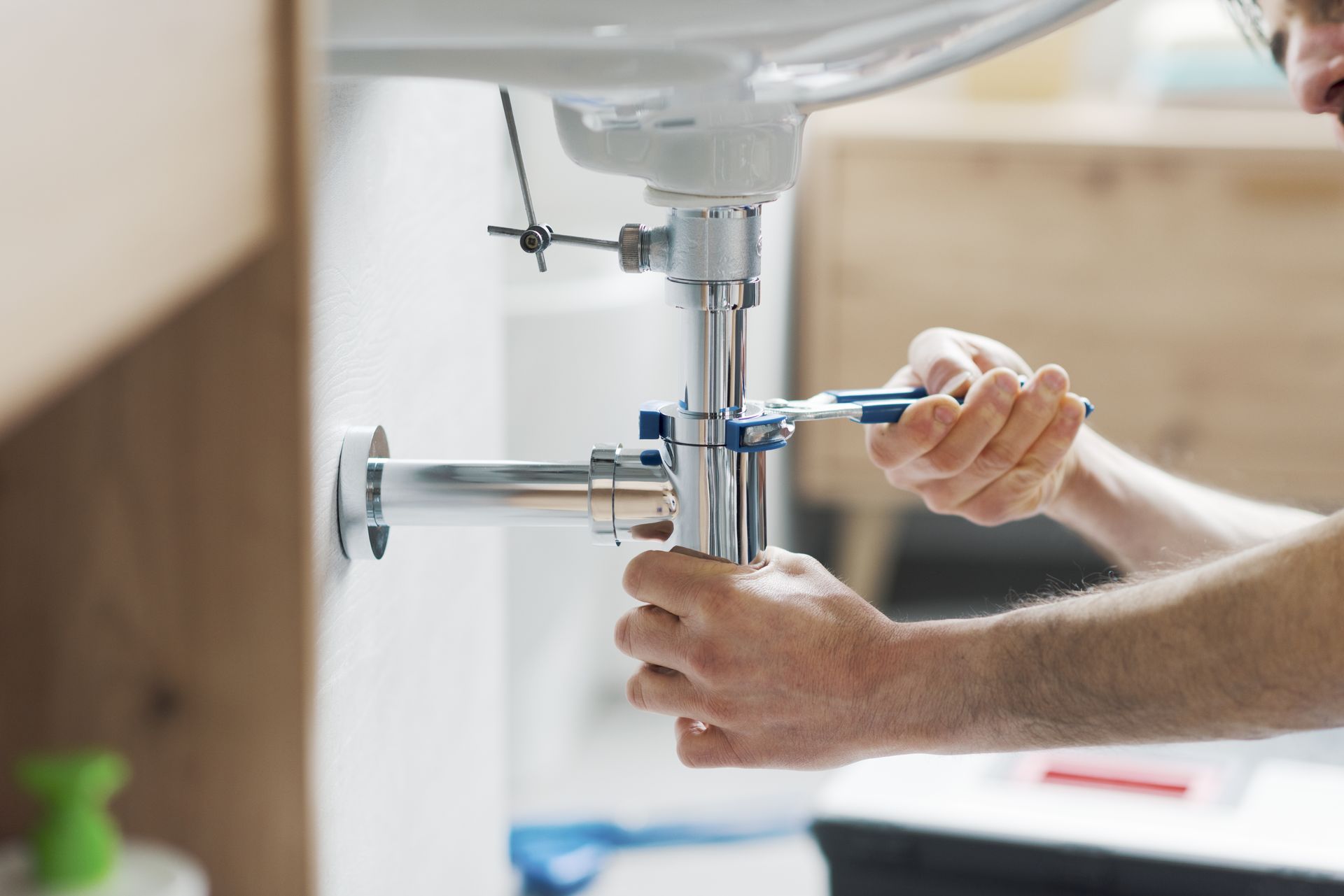 Plumber tightening a bathroom sink pipe with a wrench under a white basin