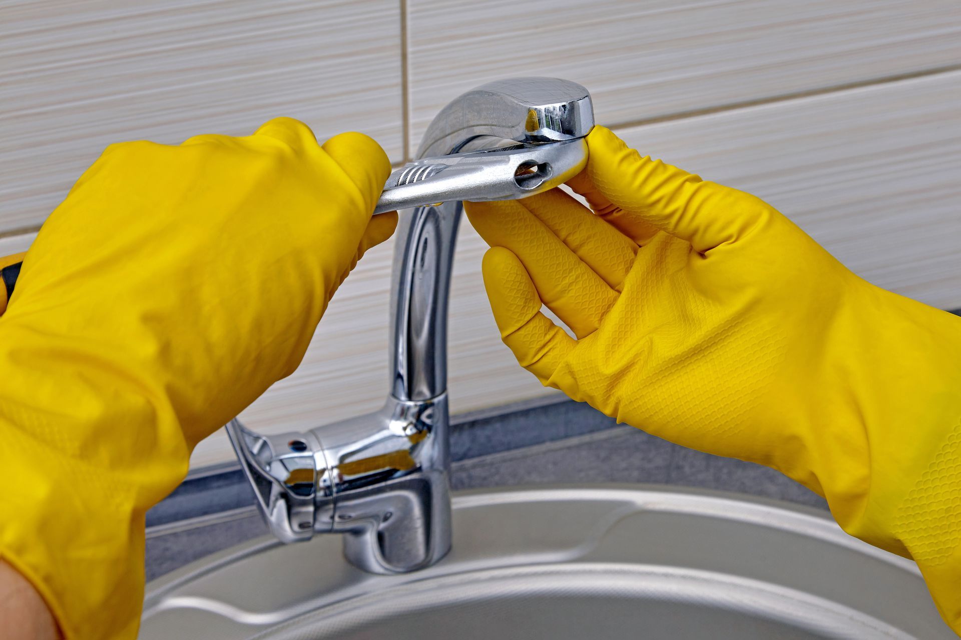 Yellow-gloved hands cleaning a chrome faucet in a sink area