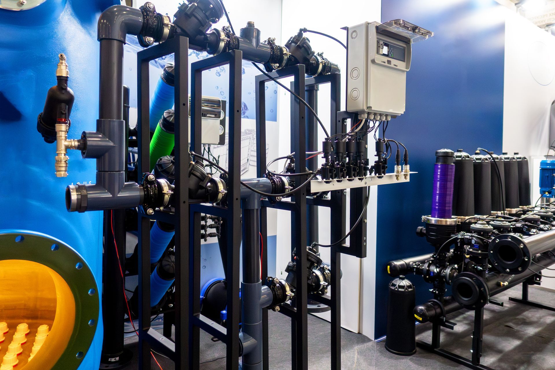 Industrial machinery with black pipes and control panels inside a factory, against a blue wall.