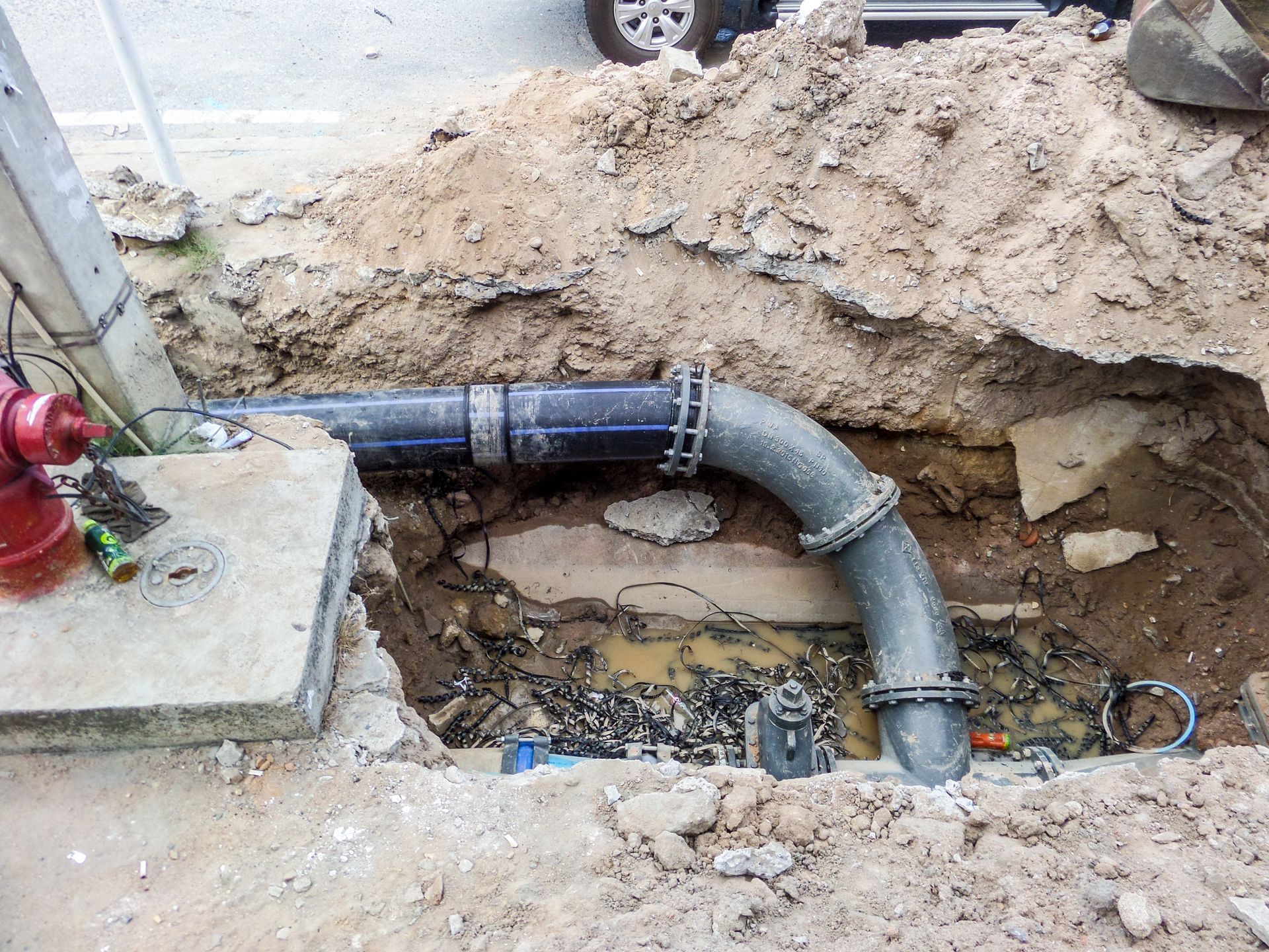Broken drainpipe in an excavated trench beside a concrete slab and muddy ground