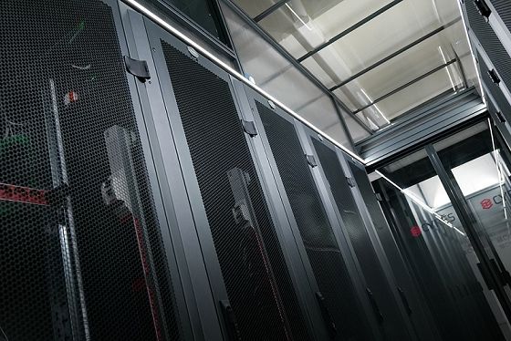 Une rangée de baies de serveurs noires dans un centre de données avec un sol métallique et des chemins de câbles aériens.