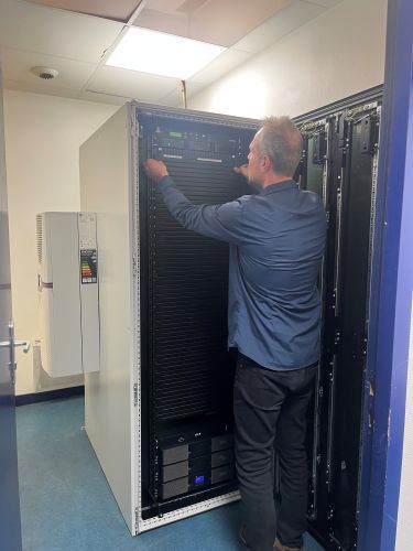 Une personne travaillant sur une baie de serveurs ouverte dans une salle informatique bien éclairée.
