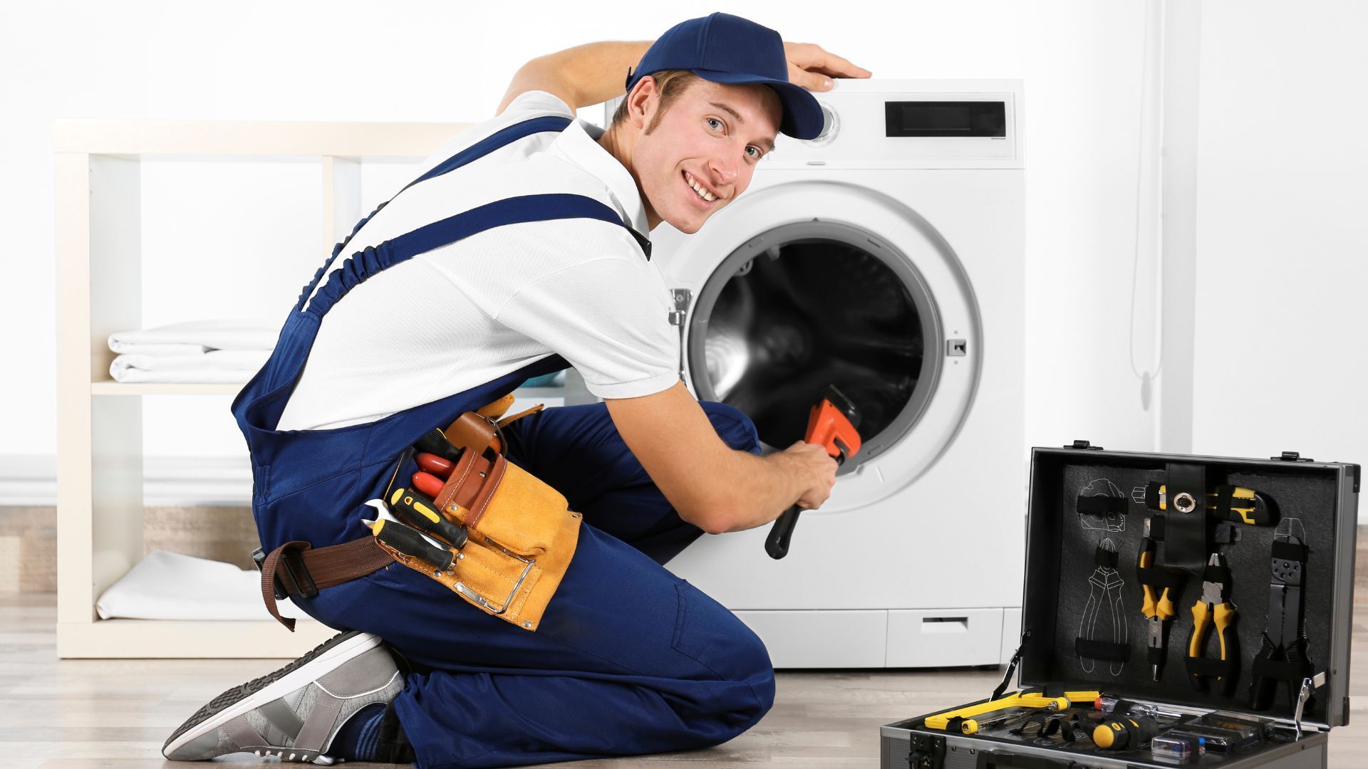 A man is fixing a washing machine with a wrench.