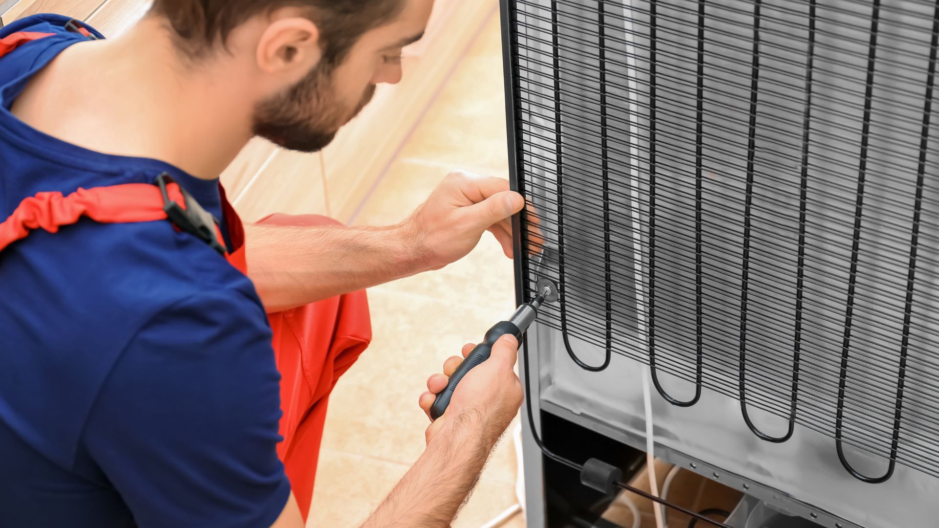 A man is fixing a refrigerator with a screwdriver.