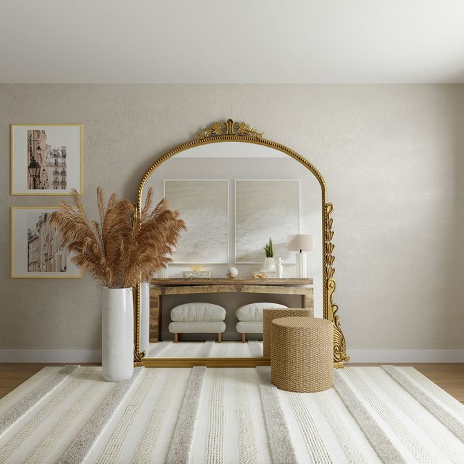 Minimal neutral room with a gold arched mirror, white vase of dried grasses, woven stool, and striped rug