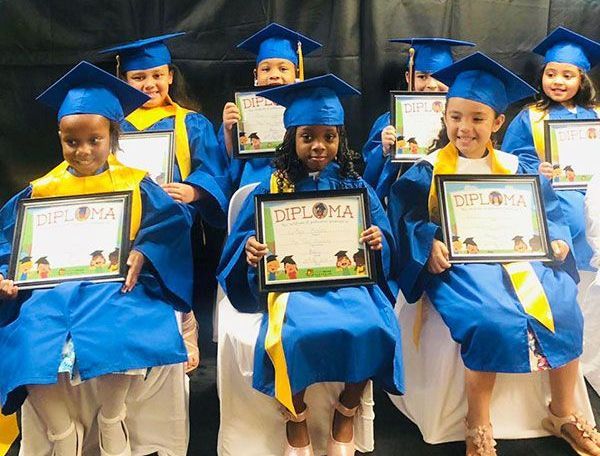 A group of young girls in graduation caps and gowns are holding diplomas.