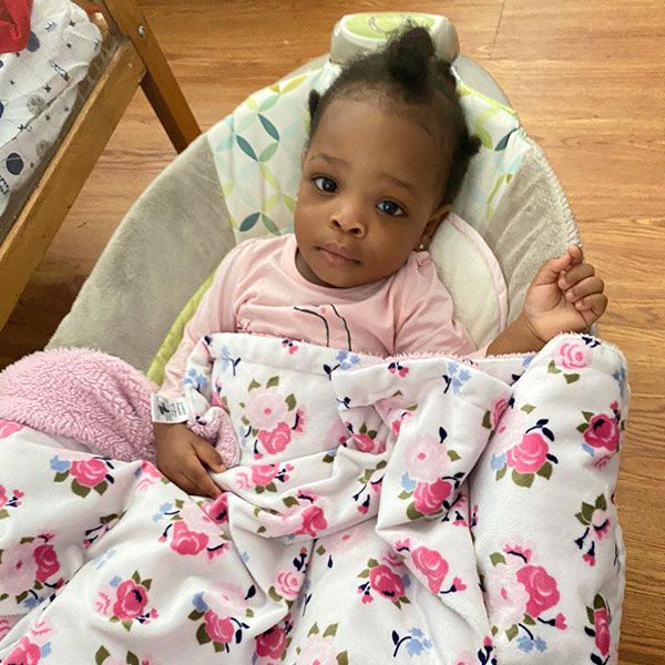 A baby is wrapped in a floral blanket and sitting in a chair.