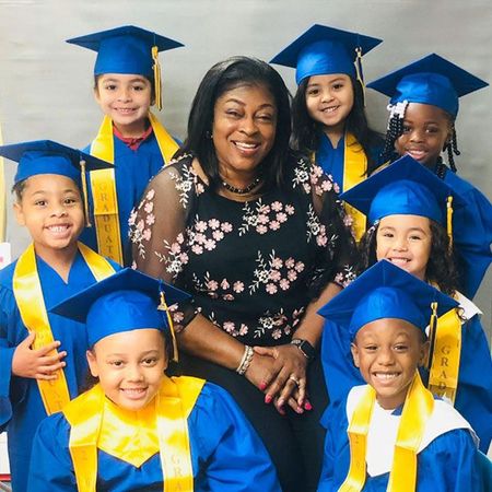 A group of children wearing graduation caps and gowns are posing for a picture with their teacher.