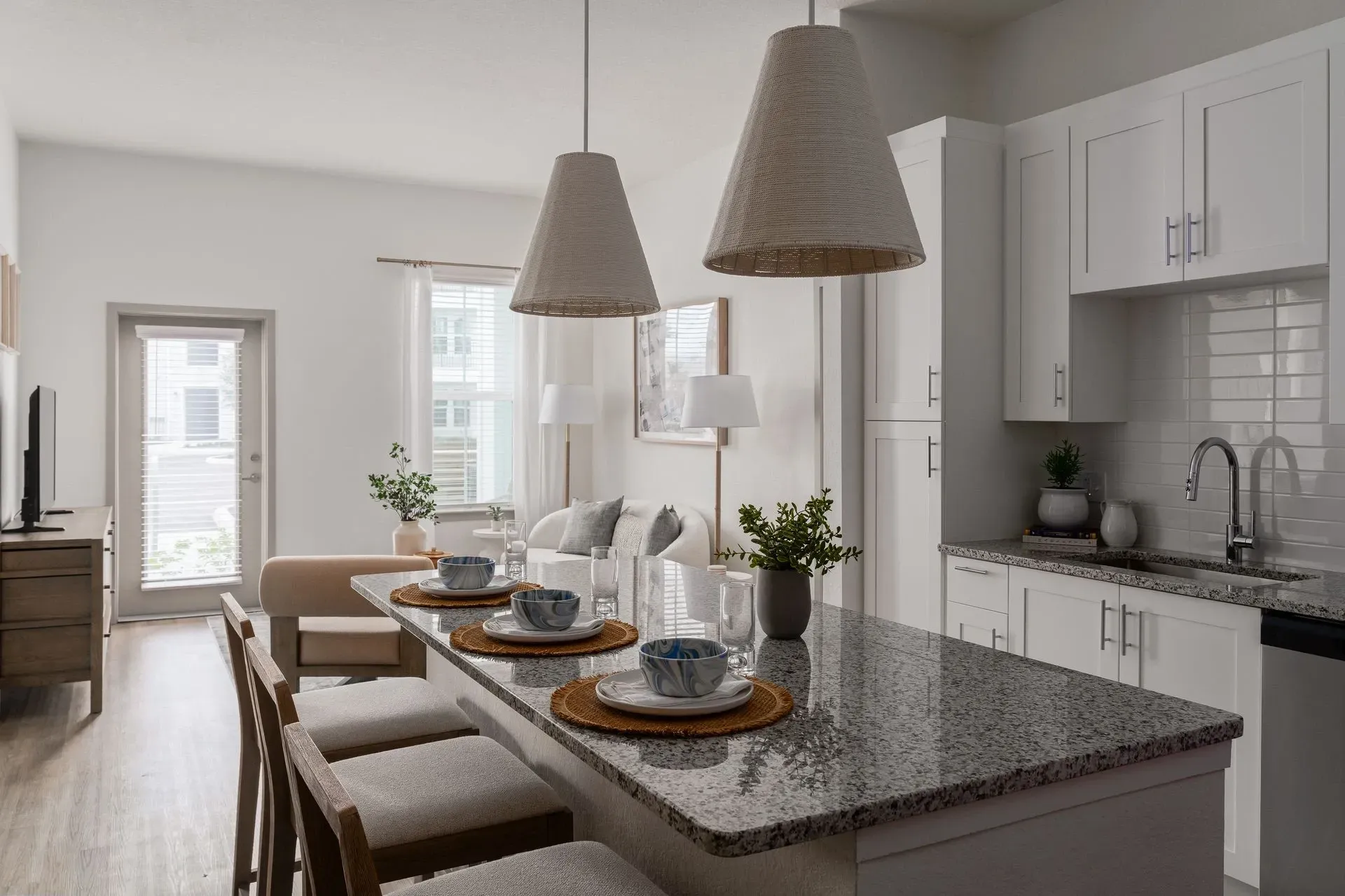 Kitchen island with granite countertops and stools, open to living area with couch and windows.