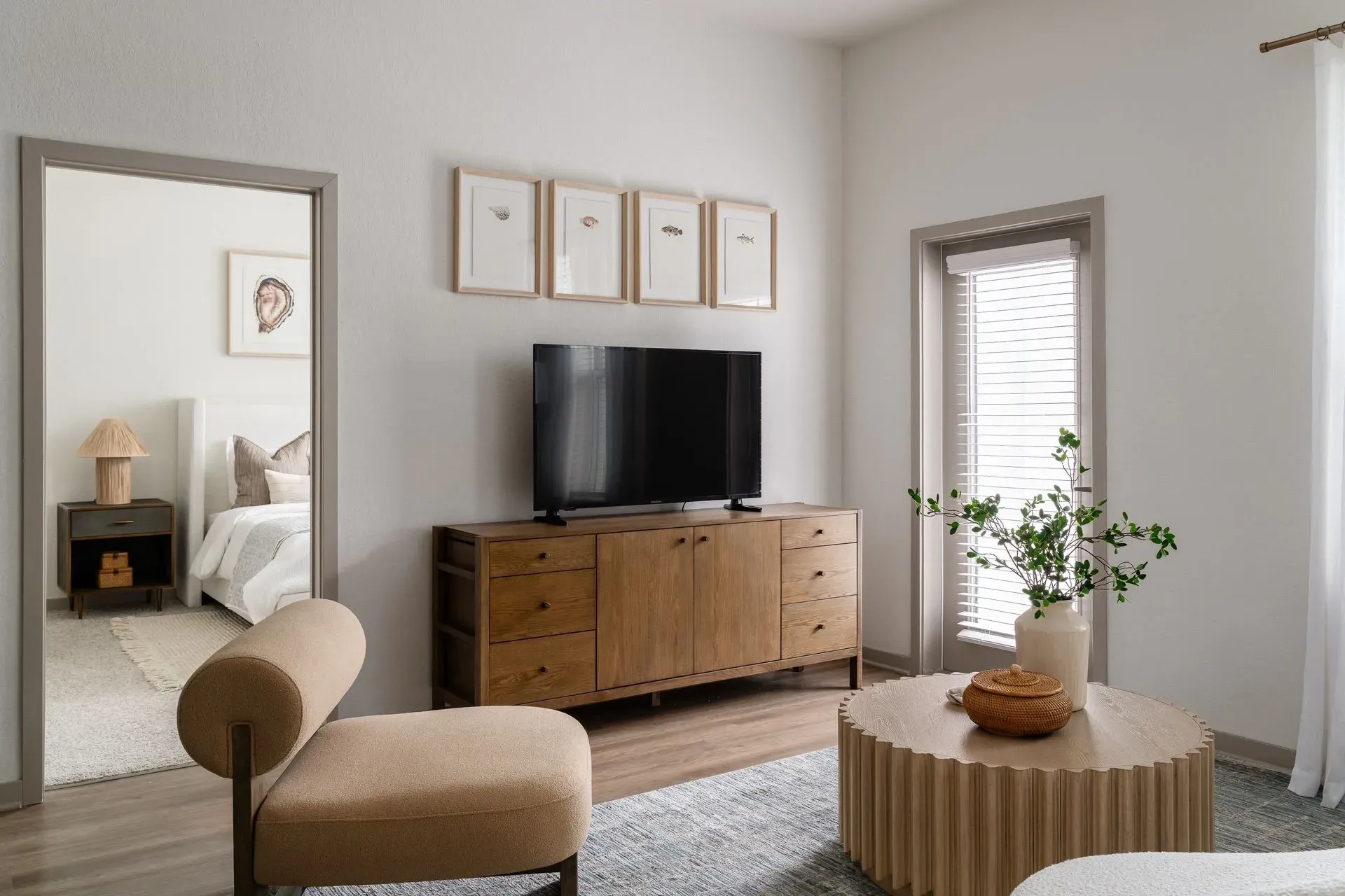 Modern living room with a television, wooden credenza, coffee table, and a glimpse into the bedroom.