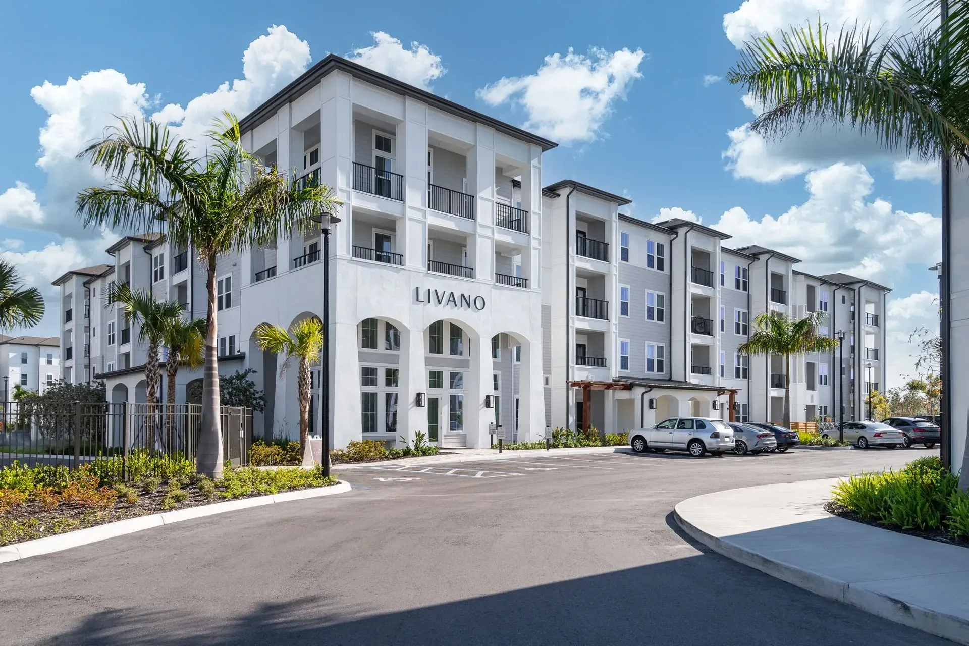 The exterior of the Livano apartment building with a manicured entrance and parking lot.