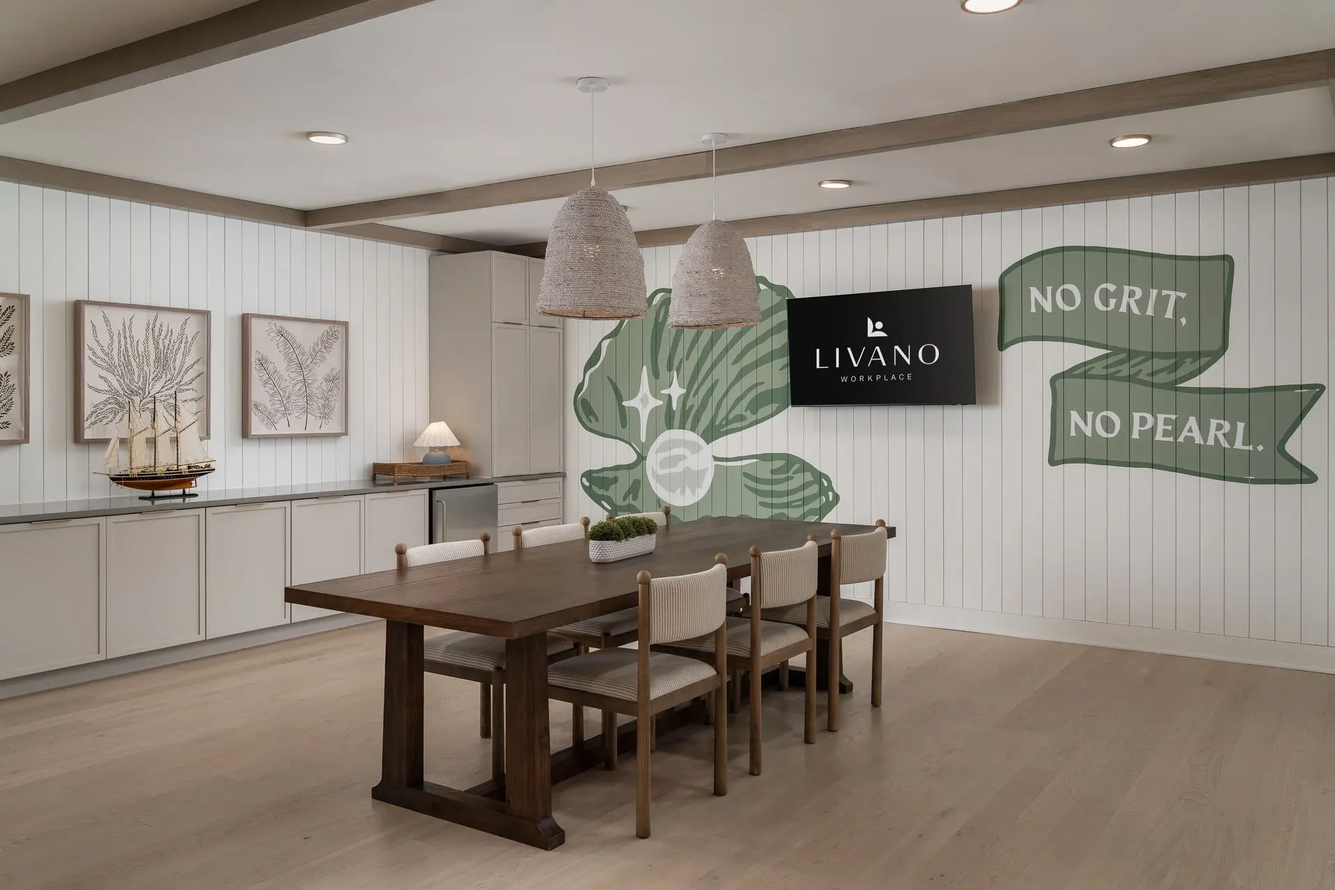 LIVANO Workplace communal dining area with a large table and chairs, a TV displaying the LIVANO logo, and nautical-themed art.