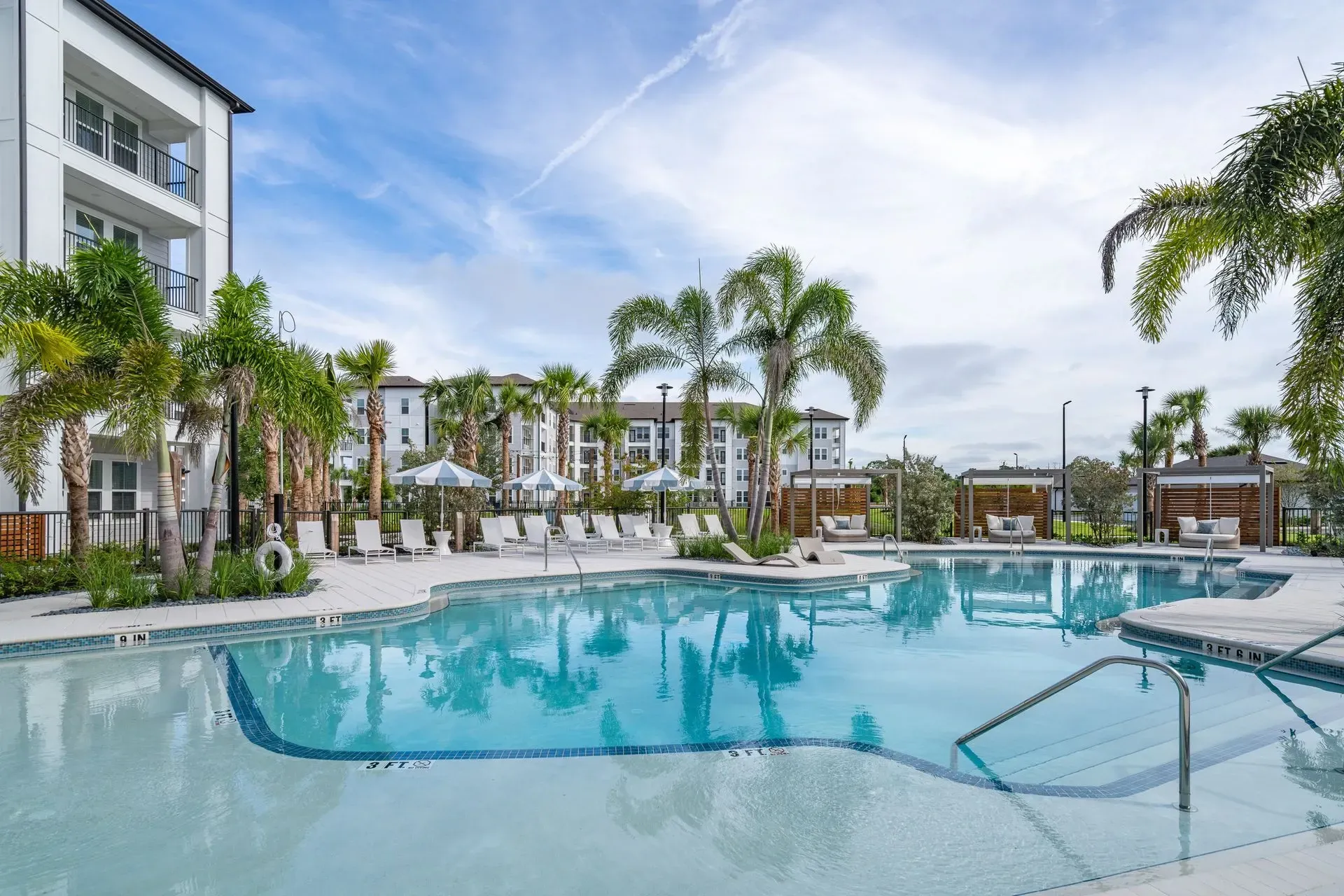 Resort-style swimming pool with lounge chairs and palm trees.