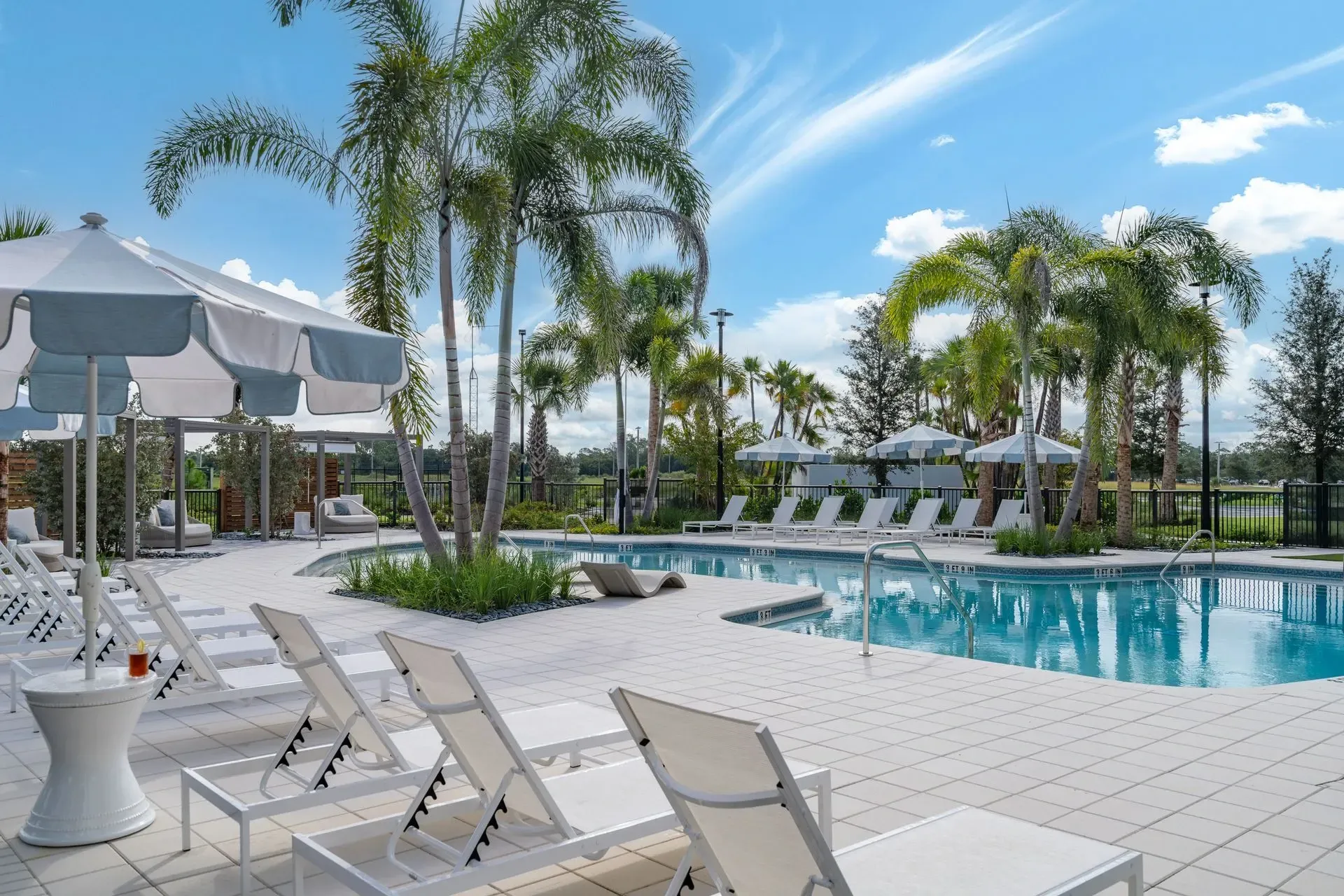 Resort-style swimming pool with lounge chairs and umbrellas, surrounded by palm trees.