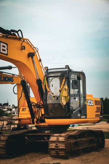 Yellow backhoe loader pushing sand on a construction site under a clear sky.