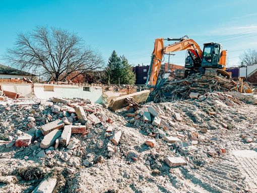 Excavator on a rubble pile at a demolition site under a clear blue sky