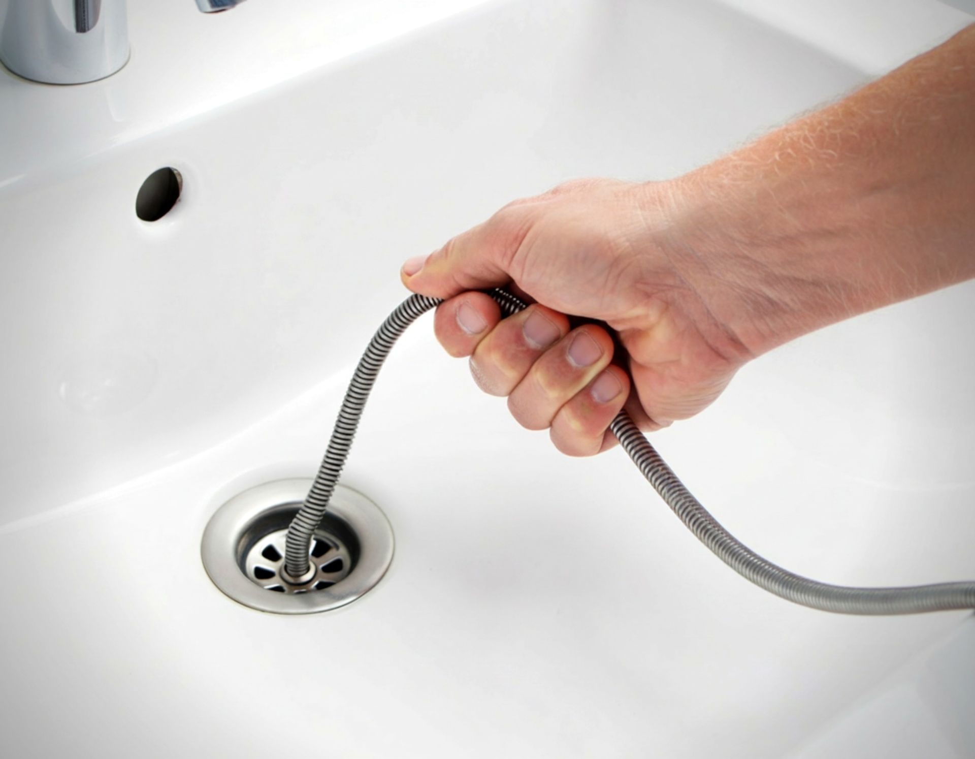Hand using a drain snake to unclog a white bathroom sink drain