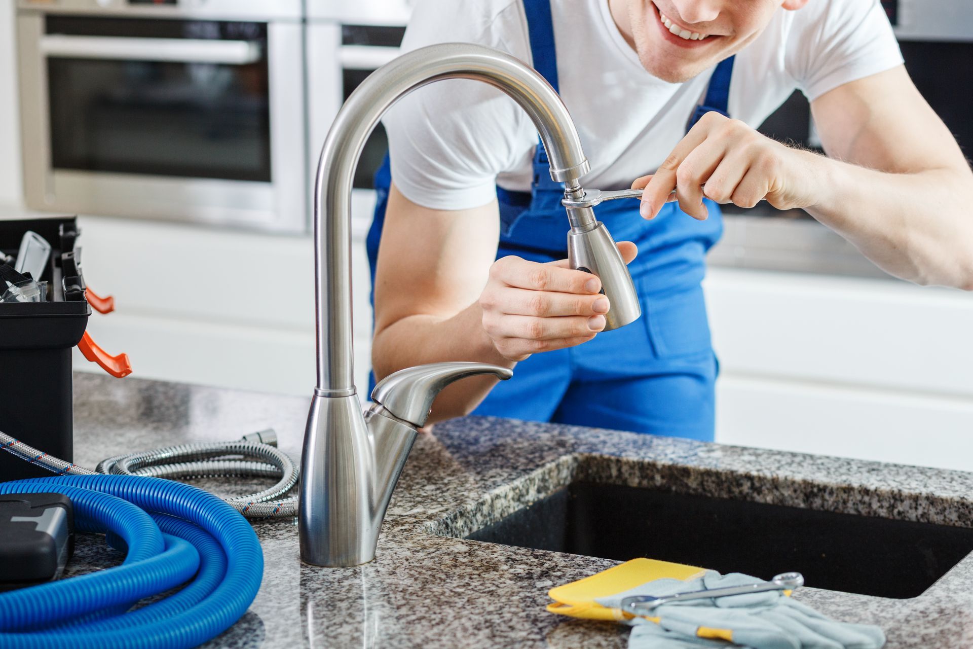 Person tightening a kitchen faucet with a wrench beside a black sink and granite countertop