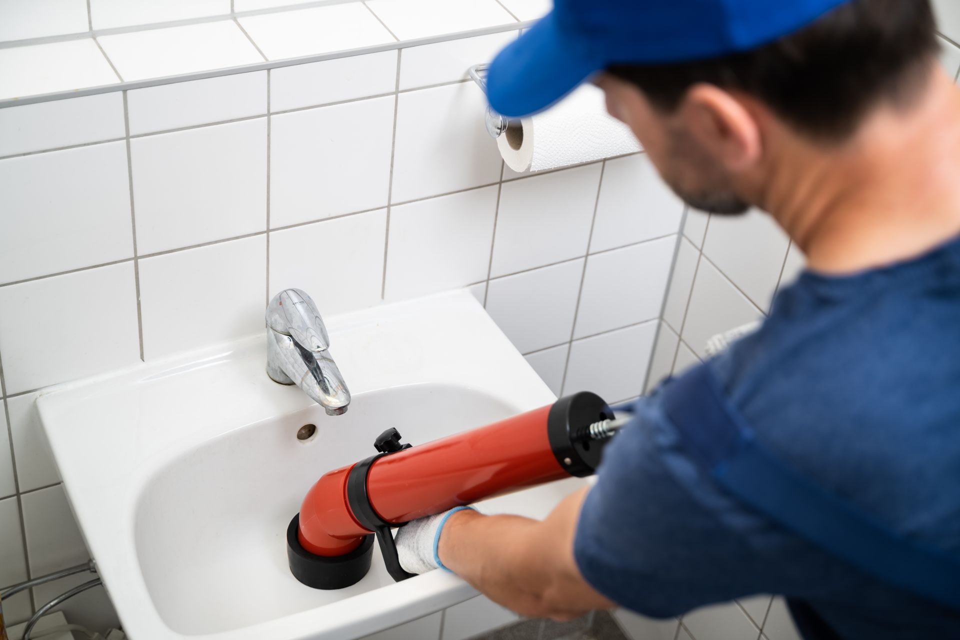 Person using a red drain-cleaning machine in a tiled bathroom sink