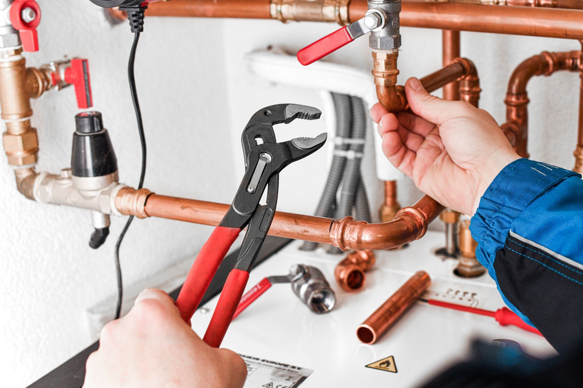 Hands using pliers to fix copper plumbing pipes with a red valve in a wall installation