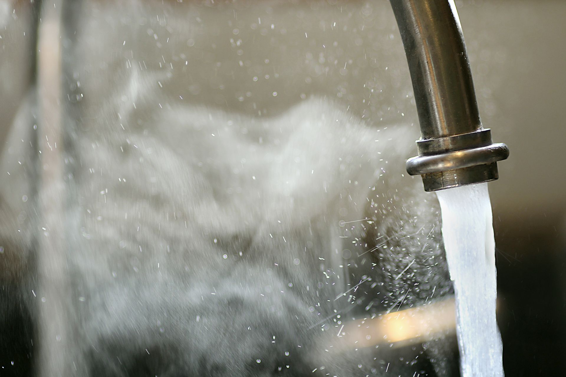 Running faucet with water splashing into a sink, creating mist and droplets