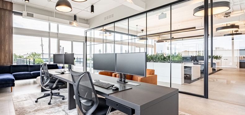 Modern office space with desks, chairs, glass walls, and natural light.