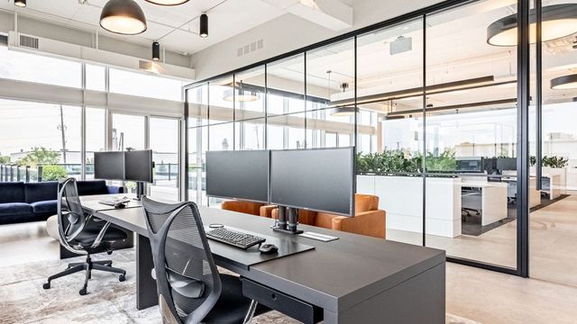 Modern office interior with workstations, glass walls, and a lounge area.