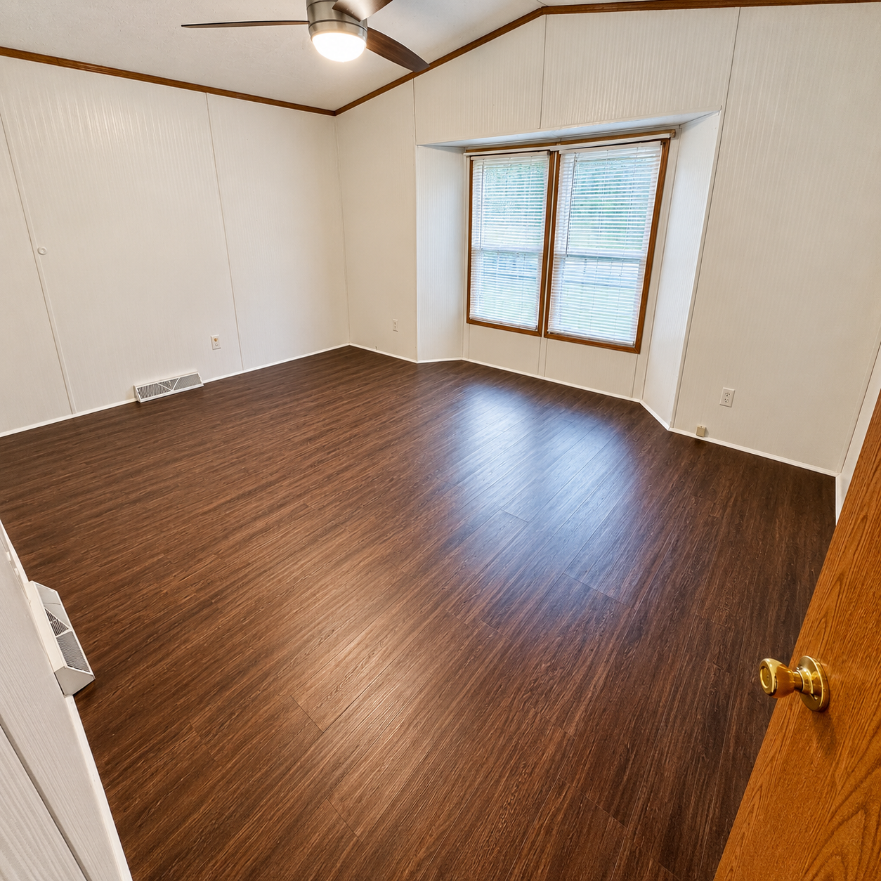 Empty room with dark wood floor, white walls, ceiling fan, and window blinds.