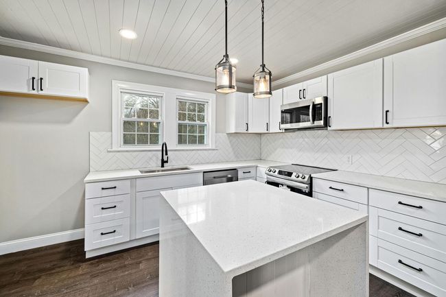 Bright white modern kitchen with island, stainless appliances, pendant lights, and wood floors