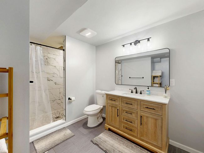 Modern bathroom with wood vanity, toilet, walk-in shower, and white walls
