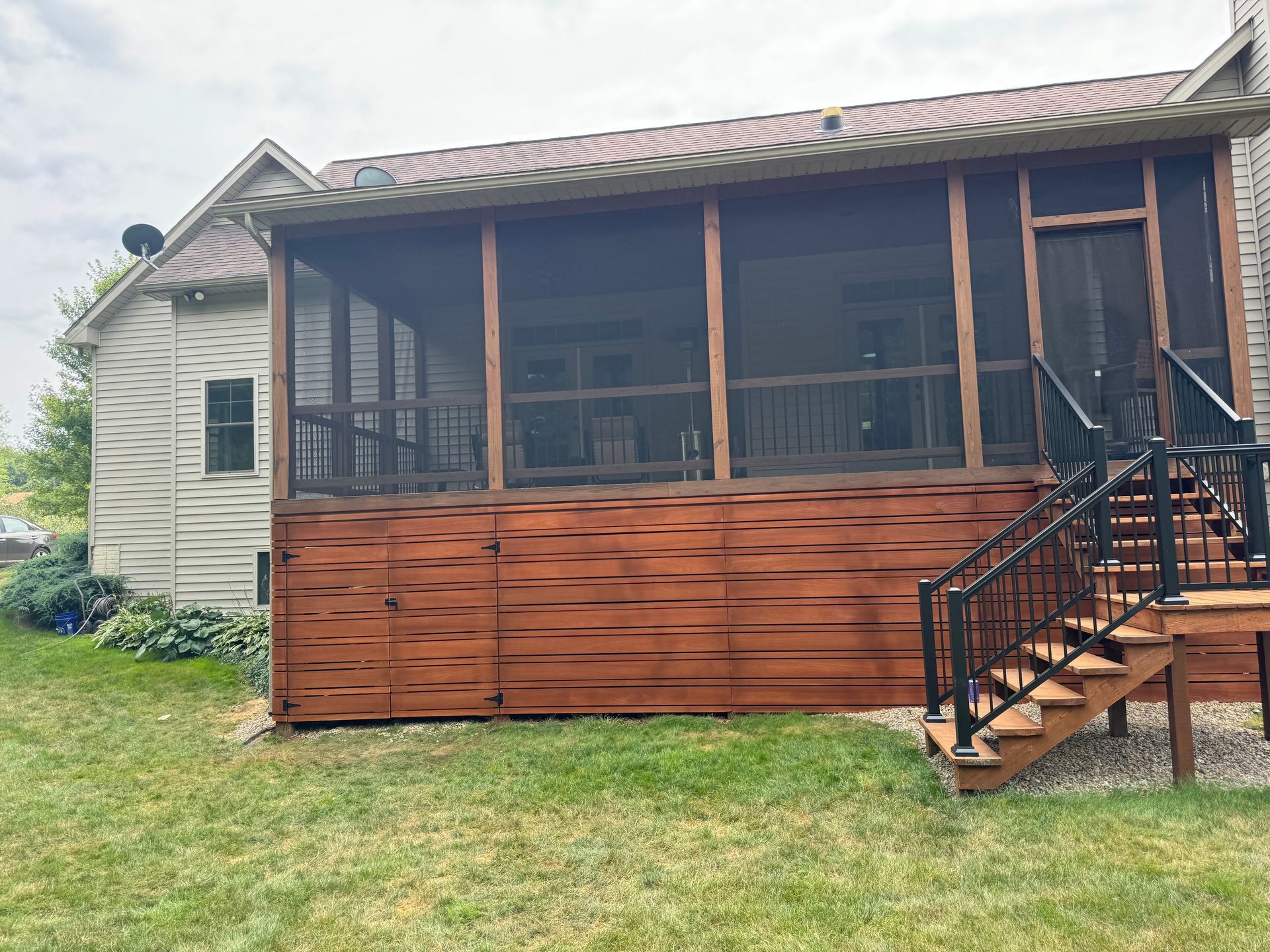 Screened porch with brown siding, black stairs, and a tiled roof on a grassy yard