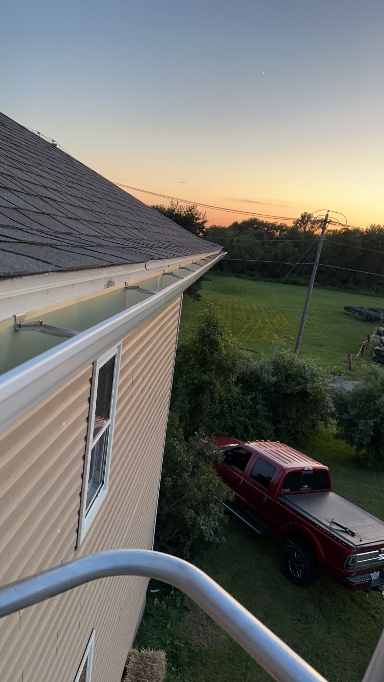 View from a rooftop over a house, lawn, and red pickup truck at sunset.