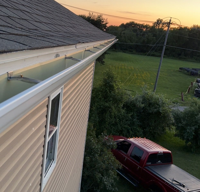 Side view of a beige house roof at sunset, with a red pickup below and a grassy yard beyond.