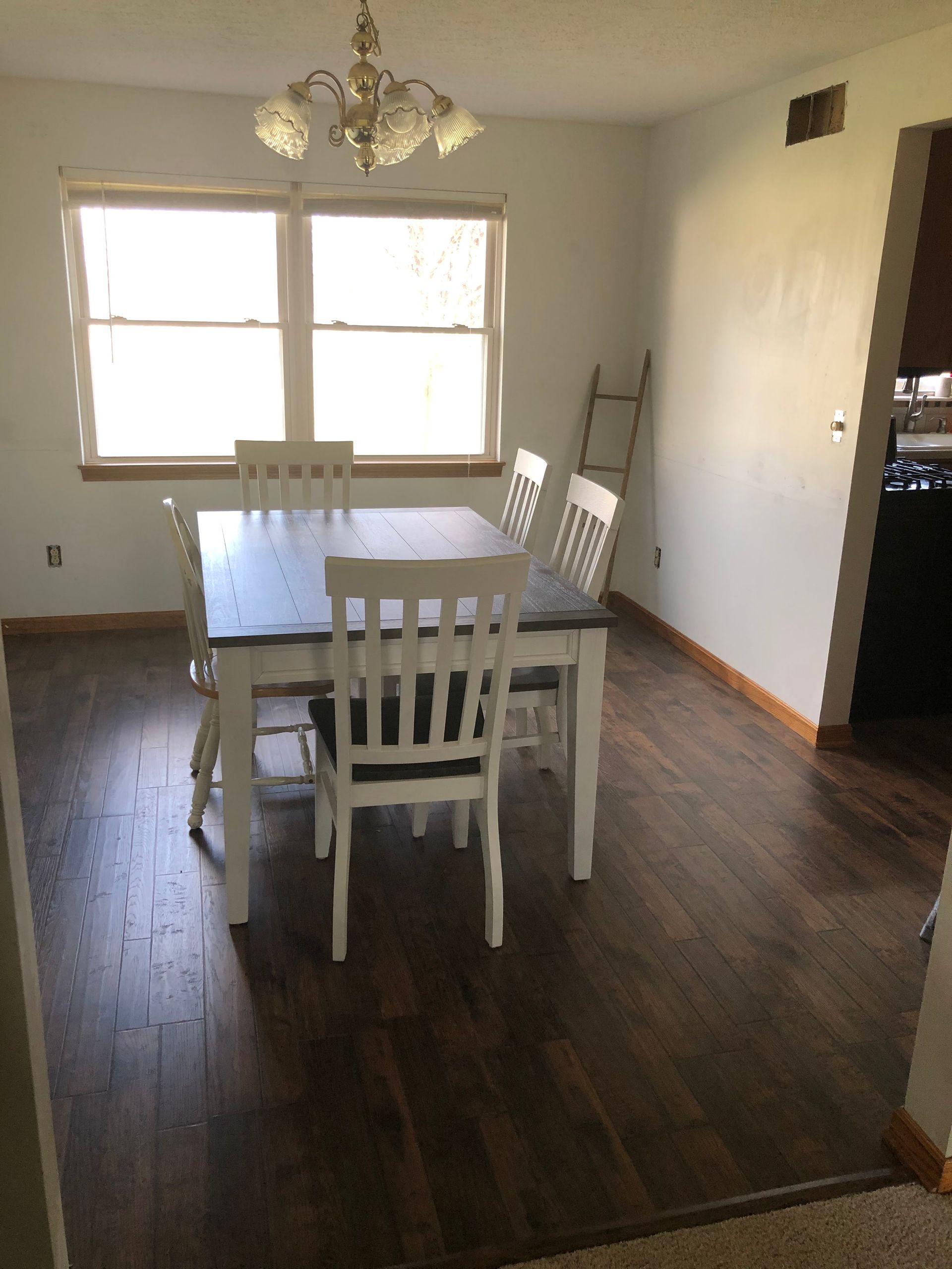 Dining room with white table and chairs, dark wood floor, and a large window letting in daylight.