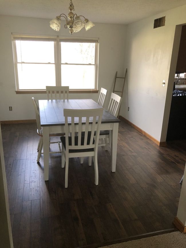 Empty dining room with white table and chairs, dark wood floors, and a large window.