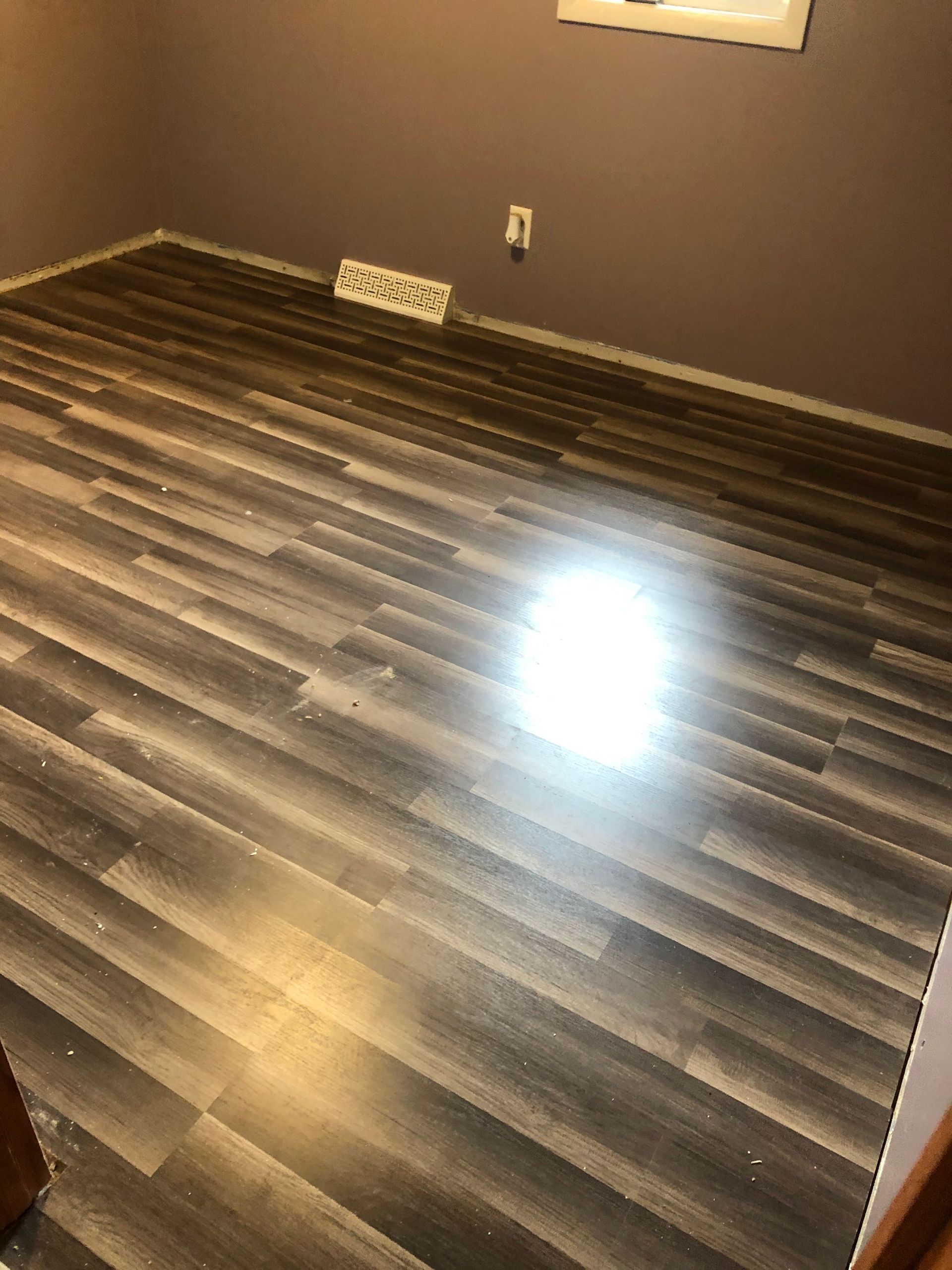 Empty room with dark wood flooring, gray walls, and a bright reflection on the floor.