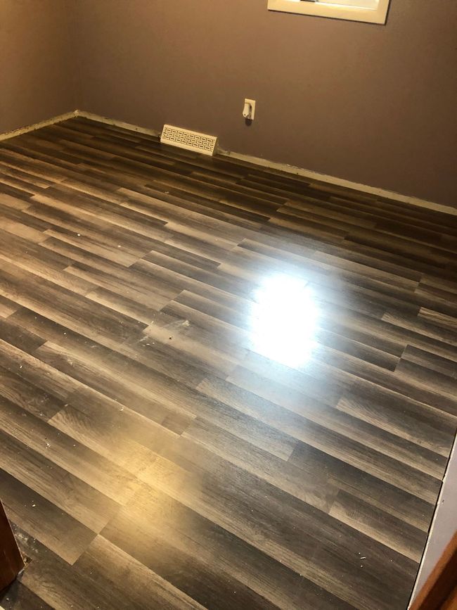 Empty room with dark wood flooring, gray walls, and a small vent on the far wall.