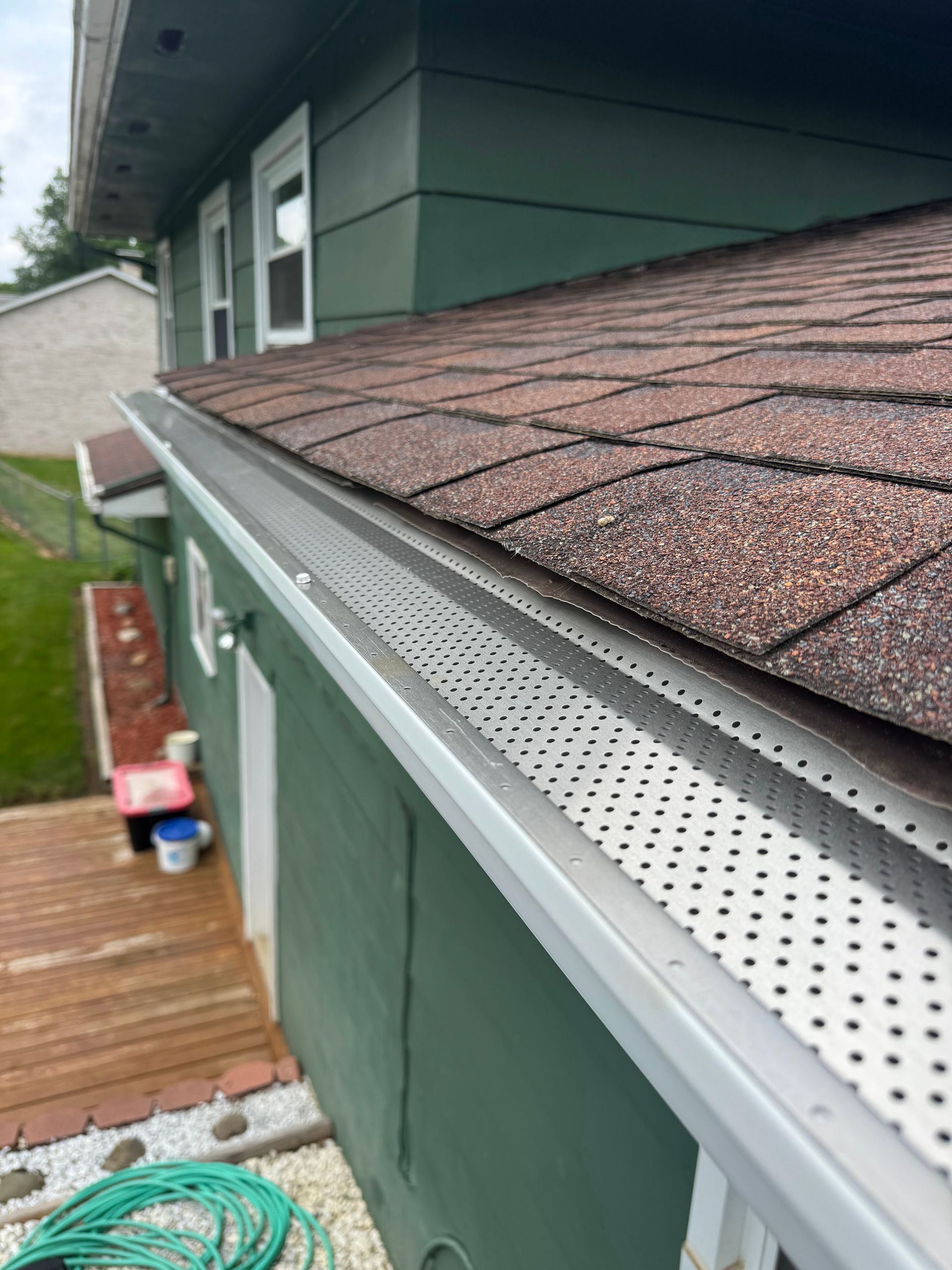 Exterior house roof with brown shingles and white gutter over a wooden deck