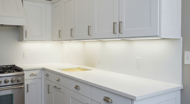 Bright white kitchen with cabinets, countertops, and a stove on the left
